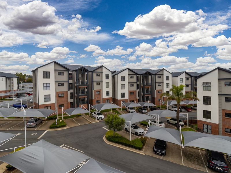 Aerial view of a modern apartment complex featuring multi-story residential buildings, paved parking areas with shade cloth carports, and landscaped grounds.