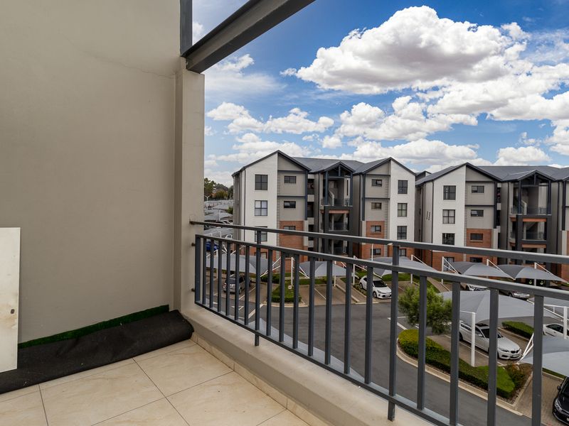 A clean, tiled balcony featuring a metal balustrade and views over the apartment complex parking area.