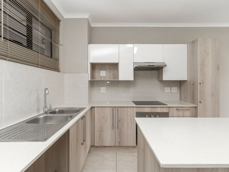 Modern kitchen featuring light wood-tone cabinetry, stone countertops, integrated stainless steel appliances, and a tiled backsplash with a double bowl sink.
