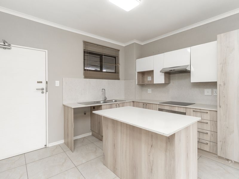 Modern kitchen featuring light wood-tone cabinetry, a central island, integrated hob with extractor, and neutral tiled finishes throughout.