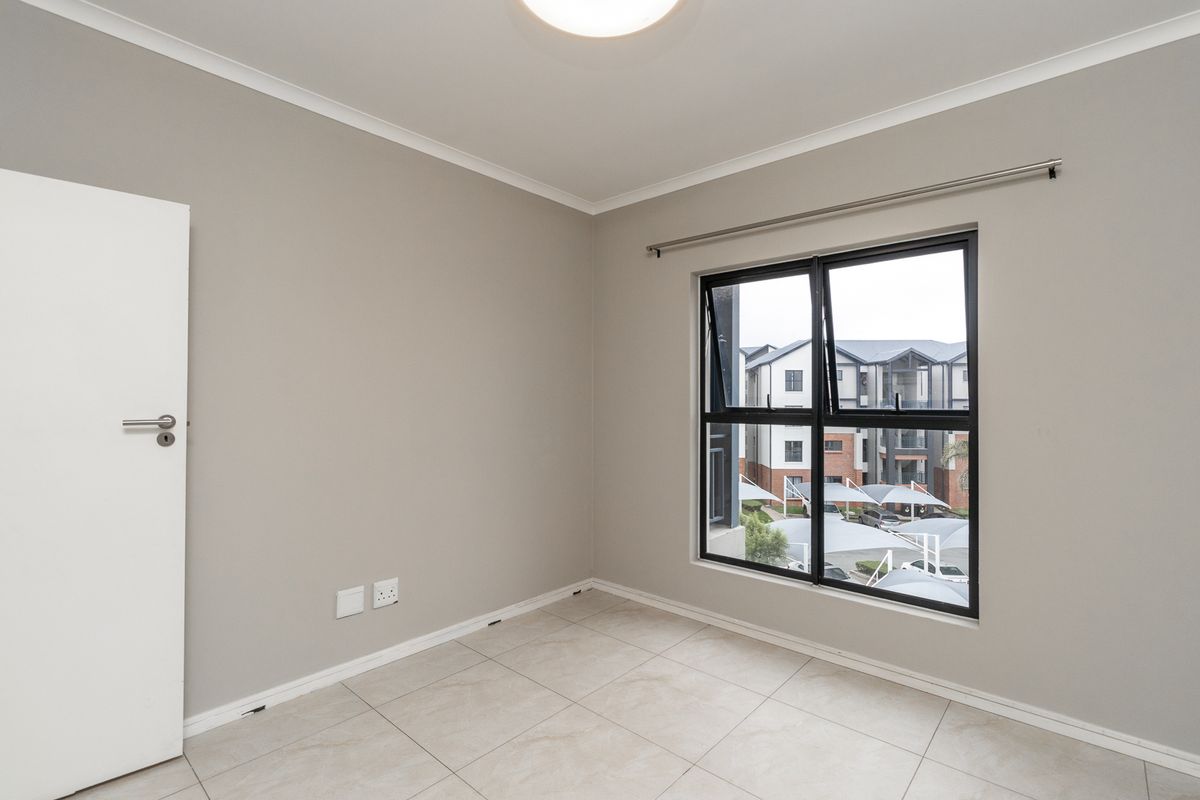 A clean, empty bedroom featuring neutral wall paint, tiled flooring, and a modern aluminium window frame with a curtain rod installed.