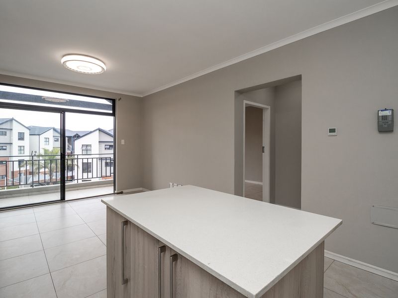Open plan living area featuring a central kitchen island, tiled flooring, and a sliding glass door leading to a balcony.