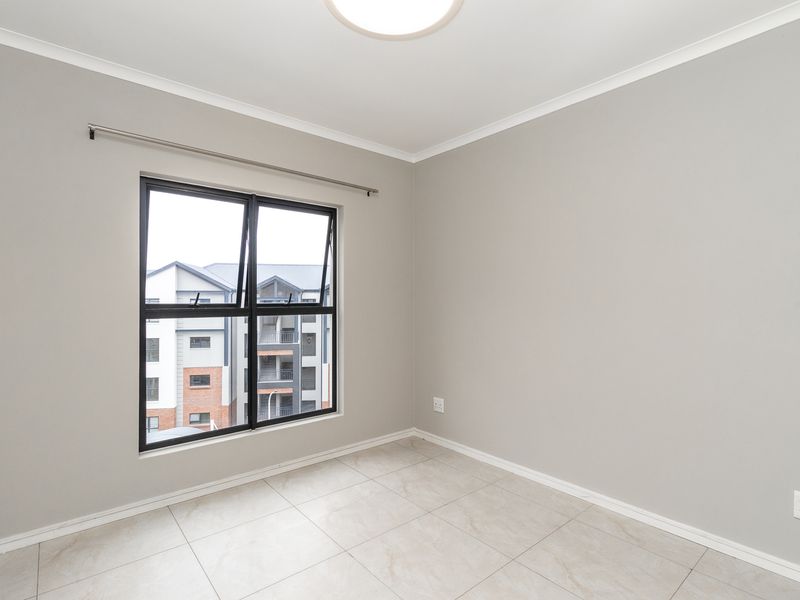 A clean, empty bedroom featuring neutral grey walls, modern tiled flooring, and a large aluminium-framed window providing natural light.