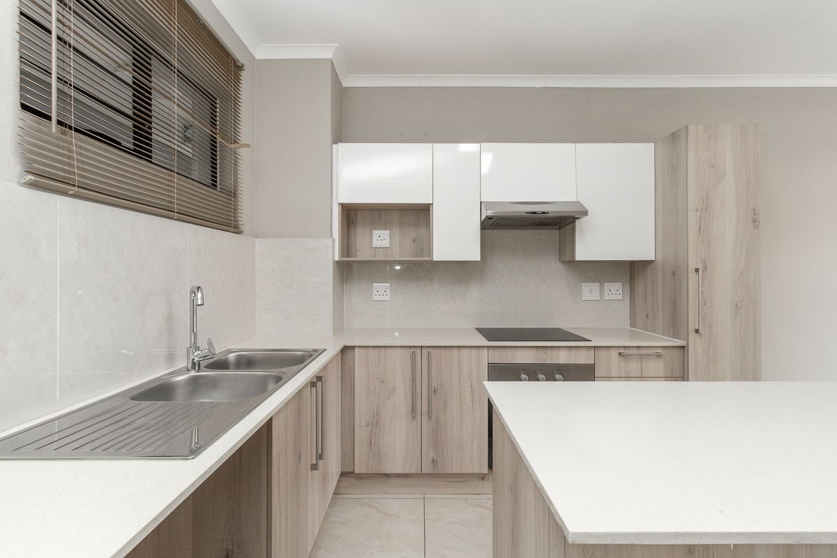 Modern kitchen featuring light wood-tone cabinetry, stone countertops, integrated stainless steel appliances, and a tiled backsplash with a double bowl sink.