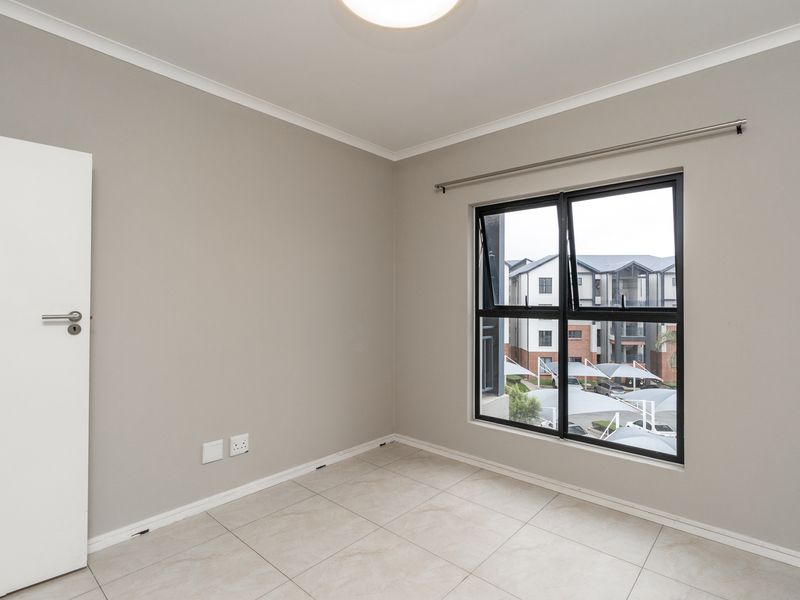 A clean, empty bedroom featuring neutral wall paint, tiled flooring, and a modern aluminium window frame with a curtain rod installed.