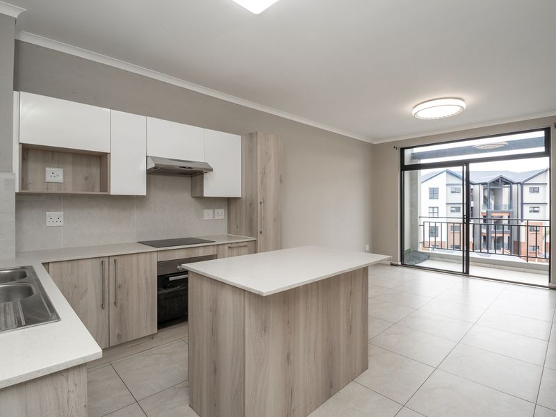 Modern open-plan kitchen featuring light wood cabinetry, stone countertops, integrated appliances, and a central island, flowing seamlessly to a private balcony.