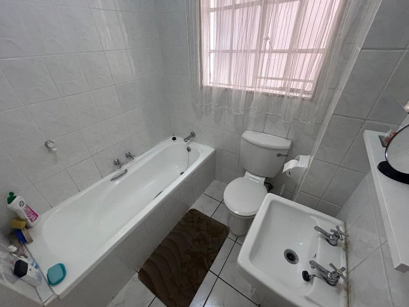 A functional bathroom featuring a standard bathtub, pedestal basin, and toilet with white wall and floor tiling.