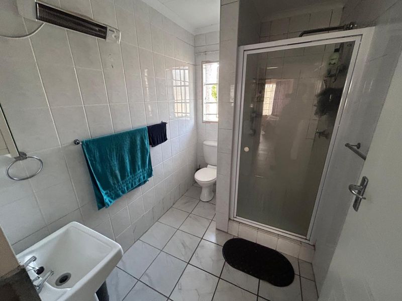A functional bathroom featuring a shower enclosure, toilet, and wall-mounted basin with tiled finishes throughout.