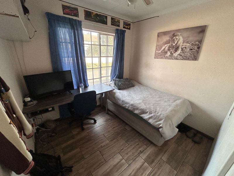 A compact bedroom featuring tiled flooring, a ceiling fan, and a window with a grid pattern, offering a functional space for rest or study.