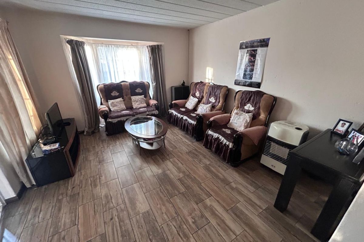 A living room featuring wood-look floor tiles, a bay window, and a textured ceiling, requiring minor cosmetic updates to improve its overall appeal.