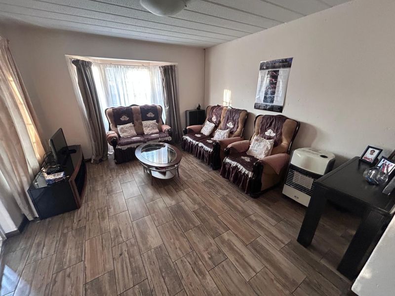 A living room featuring wood-look floor tiles, a bay window, and a textured ceiling, requiring minor cosmetic updates to improve its overall appeal.