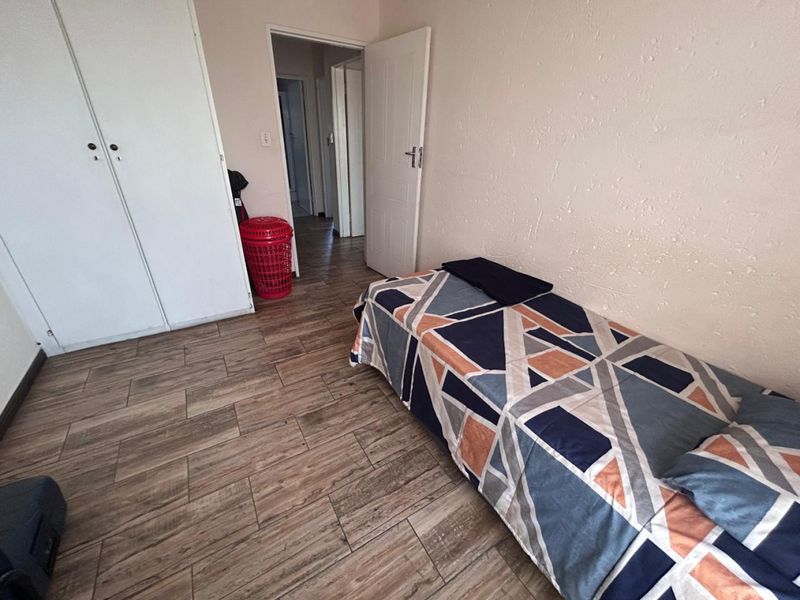 A bedroom featuring wood-look tile flooring and built-in cupboards, with access to an adjacent hallway.