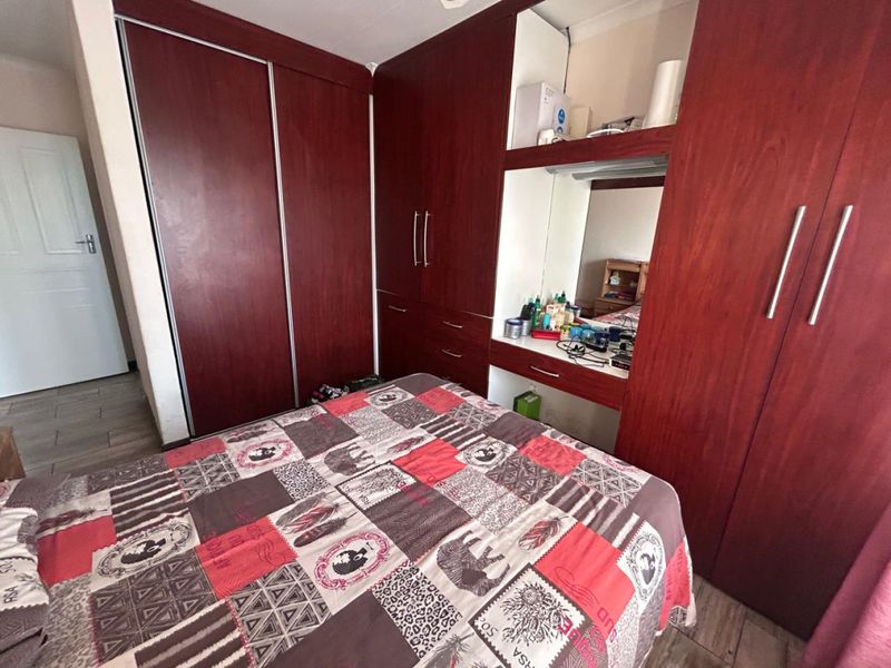 A bedroom featuring extensive dark wood built-in cupboards with an integrated vanity area and tiled flooring.