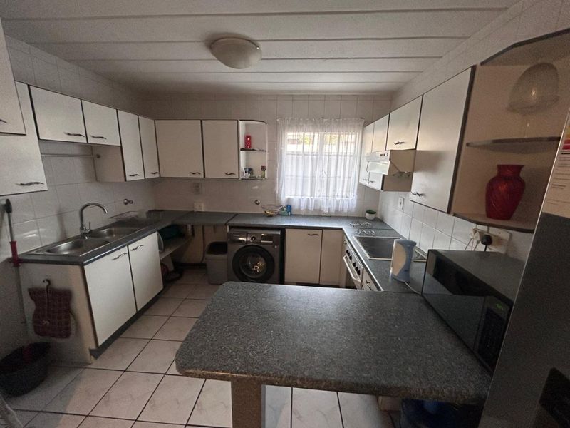 A functional kitchen featuring white cabinetry, laminate countertops, tiled flooring, and integrated laundry plumbing, offering a practical layout with potential for modern updates.
