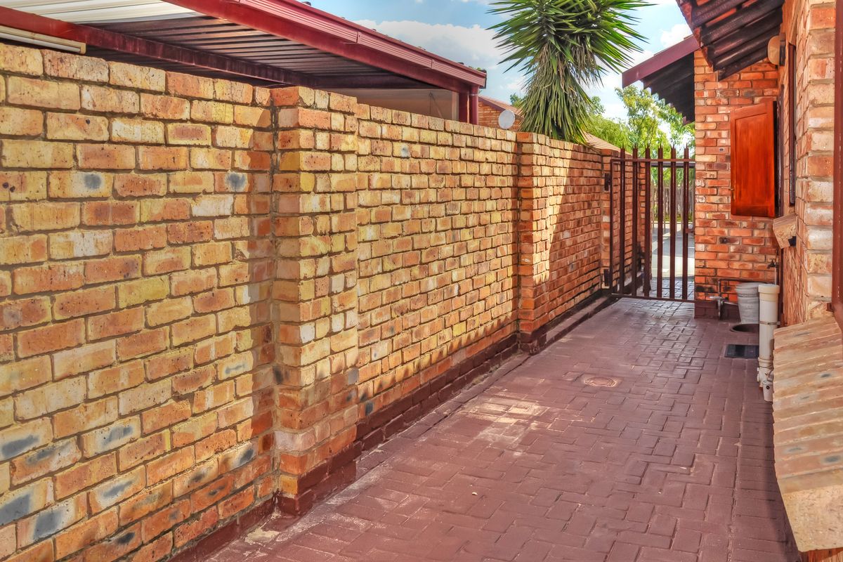 A side walkway featuring face brick boundary walls, paved flooring, and a metal security gate leading to the rear of the townhouse property.