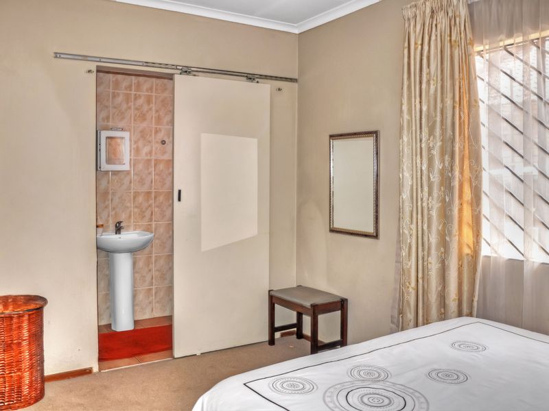 Bedroom featuring a sliding door leading to an en-suite area with a pedestal basin and tiled splashback, complemented by security bars on the window.