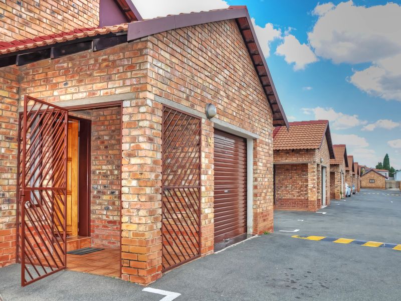 A well-maintained townhouse exterior featuring face brick construction, a roll-up garage door, and a secure entrance with a metal security gate.