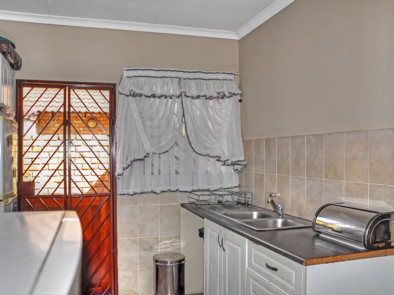 A functional scullery area featuring a double stainless steel sink, tiled splashback, laminate countertops, and built-in cabinetry with direct access to an exterior security gate.