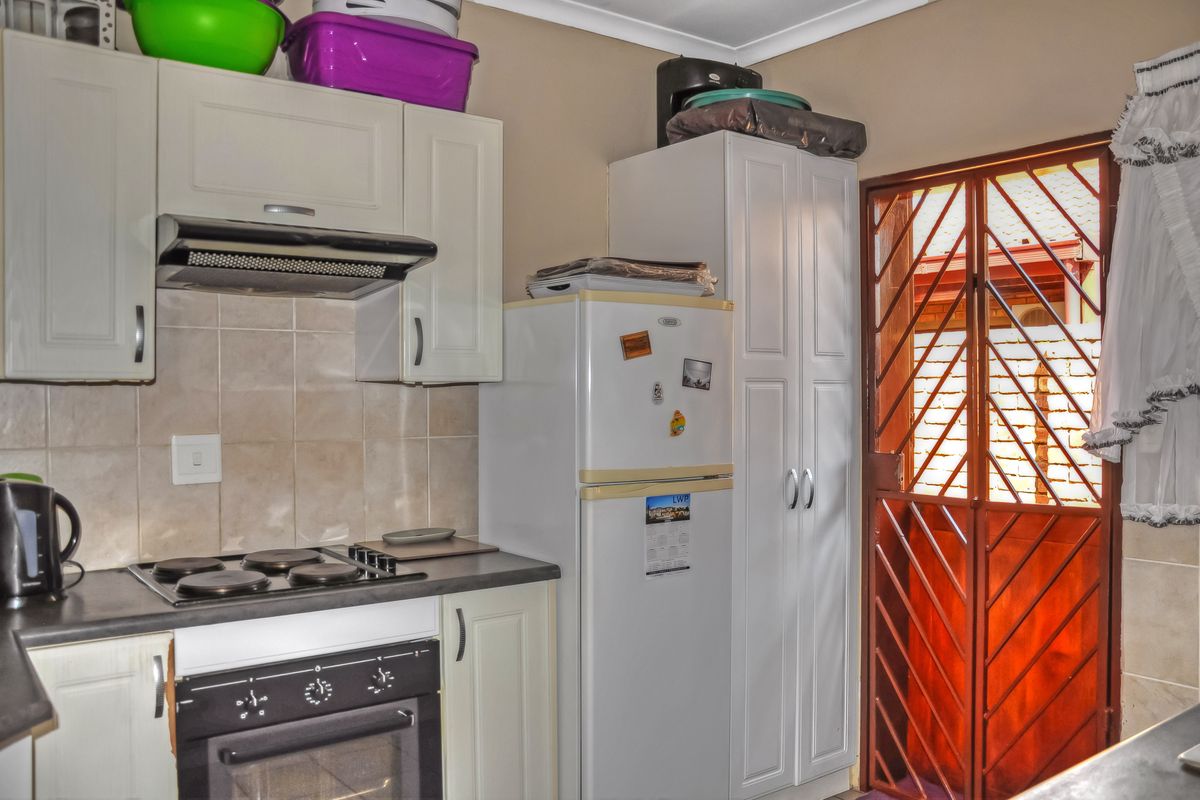 Compact kitchen featuring white cabinetry, built-in oven and hob, tiled backsplash, and direct access to the exterior via a security gate.