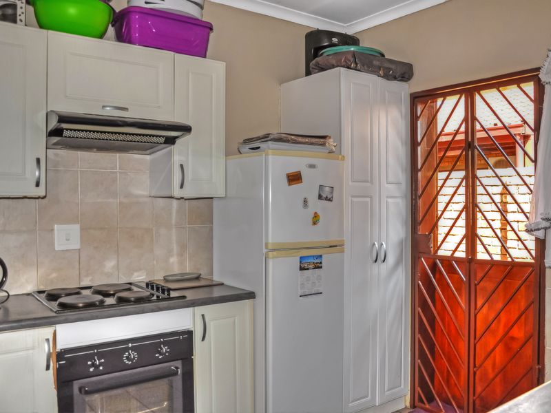 Compact kitchen featuring white cabinetry, built-in oven and hob, tiled backsplash, and direct access to the exterior via a security gate.