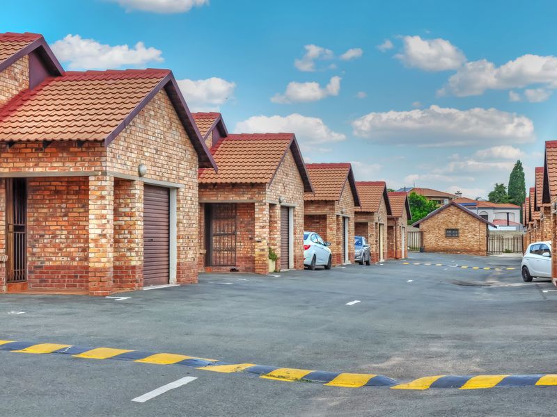 A row of face-brick townhouse garages with tiled roofs and paved driveway access in a well-maintained residential complex.