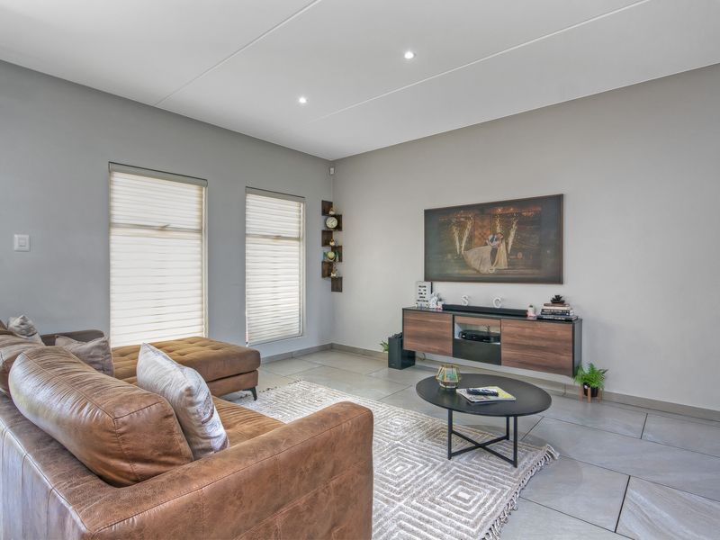 A modern, well-lit living room featuring large format floor tiles, recessed ceiling lighting, and dual windows with fitted roller blinds.
