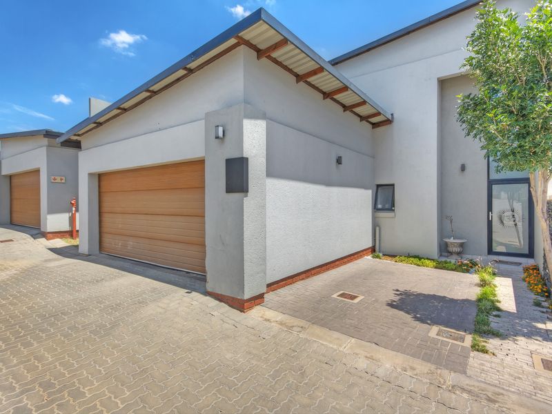 Modern townhouse exterior featuring a paved driveway, integrated garage with wooden door, and stone-clad entrance detail.
