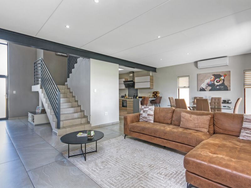 Spacious open-plan living area featuring tiled floors, a modern staircase with metal railings, an exposed steel beam, and an integrated kitchen.