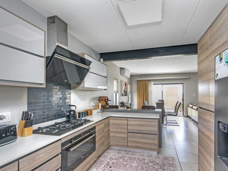 Modern open-plan kitchen featuring wood-grain cabinetry, stone countertops, gas cooktop, and integrated appliances, flowing seamlessly into the adjacent dining and living area.