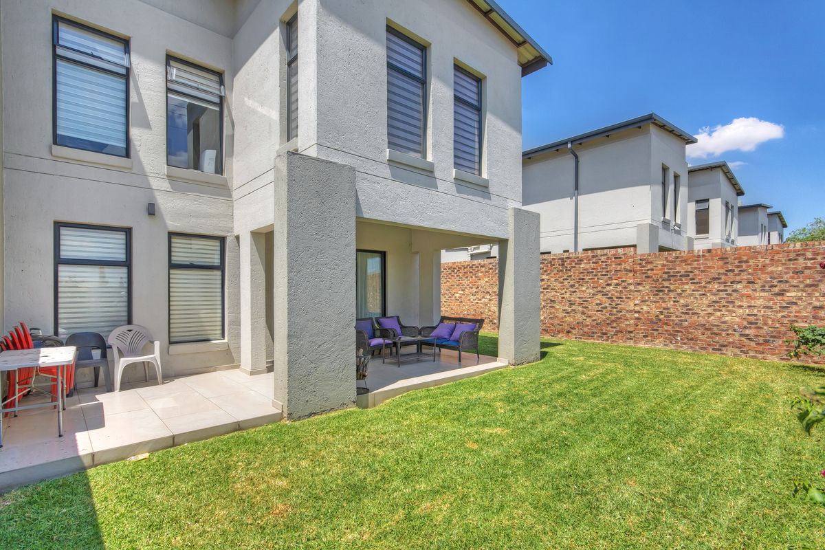 Rear view of the townhouse featuring a covered patio area, tiled flooring, and a private garden with a brick boundary wall.