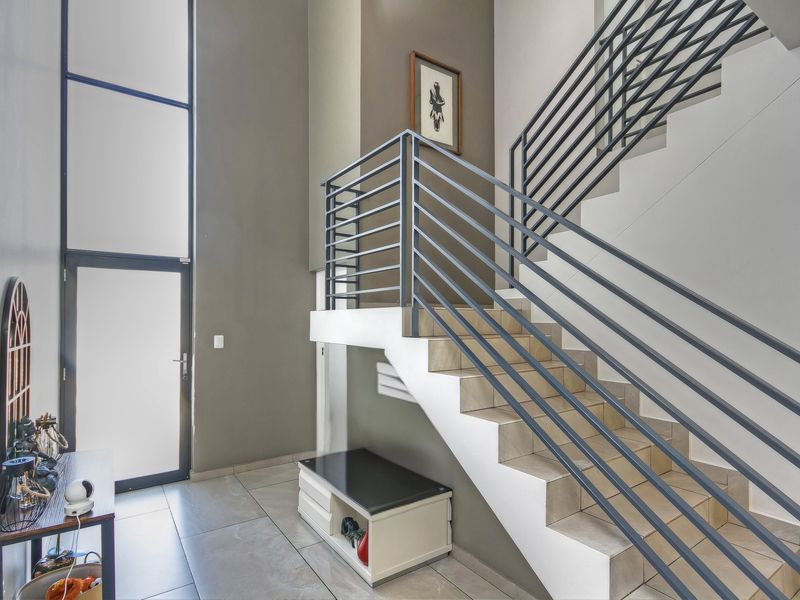 Modern entrance hall featuring a striking staircase with metal balustrades, large windows for natural light, and neutral tiled flooring.