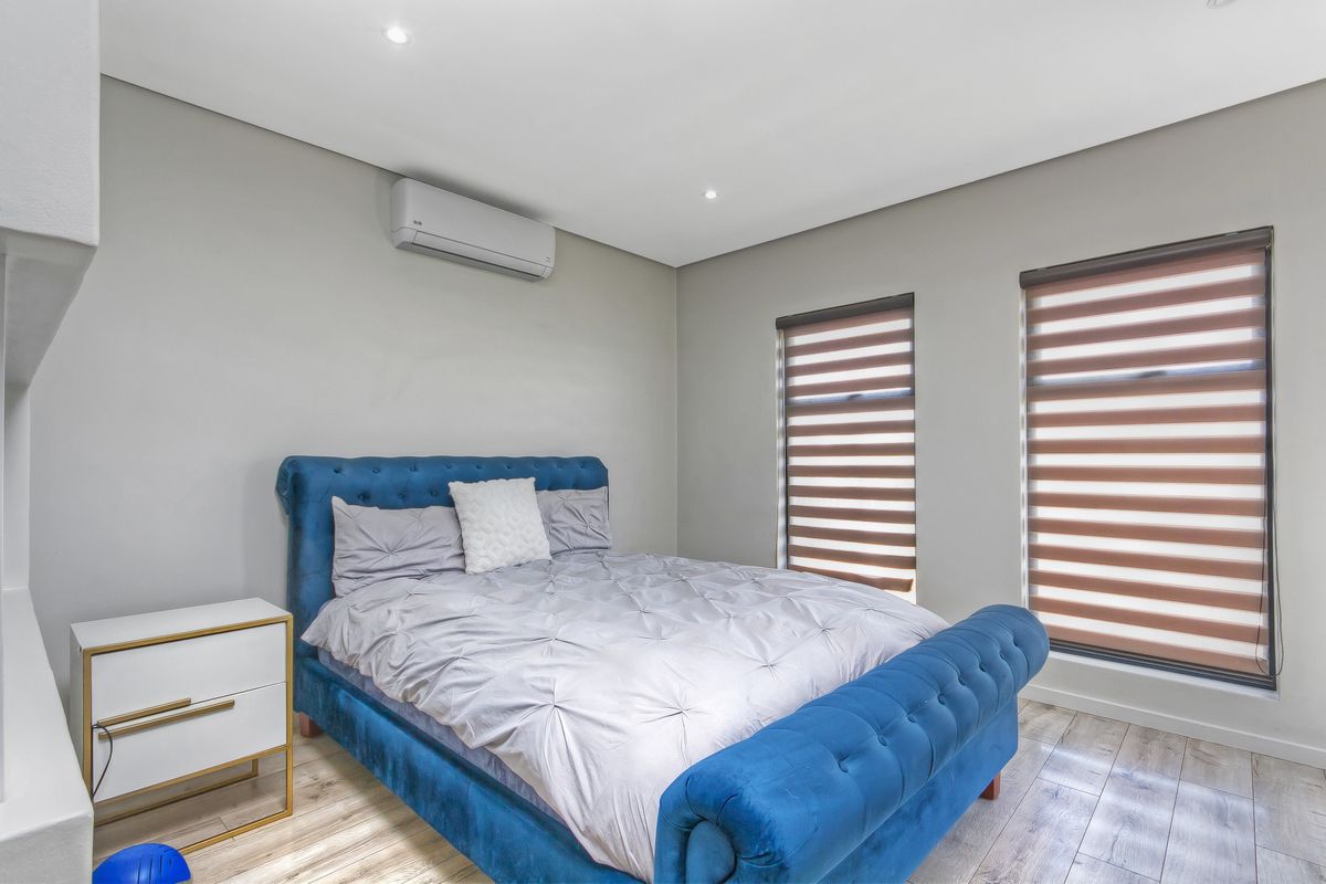 A well-maintained bedroom featuring modern laminate flooring, recessed downlighting, dual roller blinds, and a wall-mounted split-system air conditioning unit.