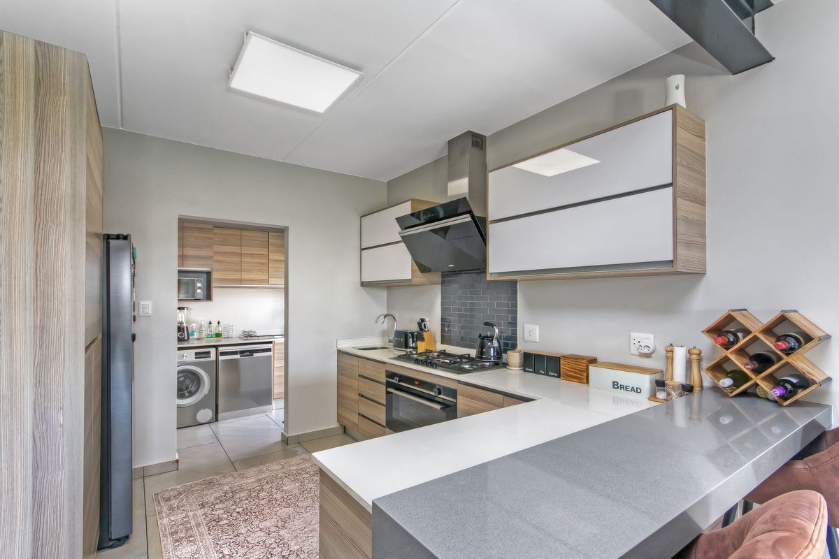 Modern kitchen featuring wood-tone cabinetry, stone countertops, integrated gas hob, and a convenient adjoining scullery area with laundry facilities.