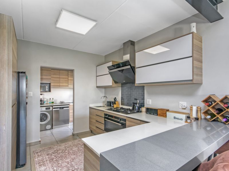 Modern kitchen featuring wood-tone cabinetry, stone countertops, integrated gas hob, and a convenient adjoining scullery area with laundry facilities.