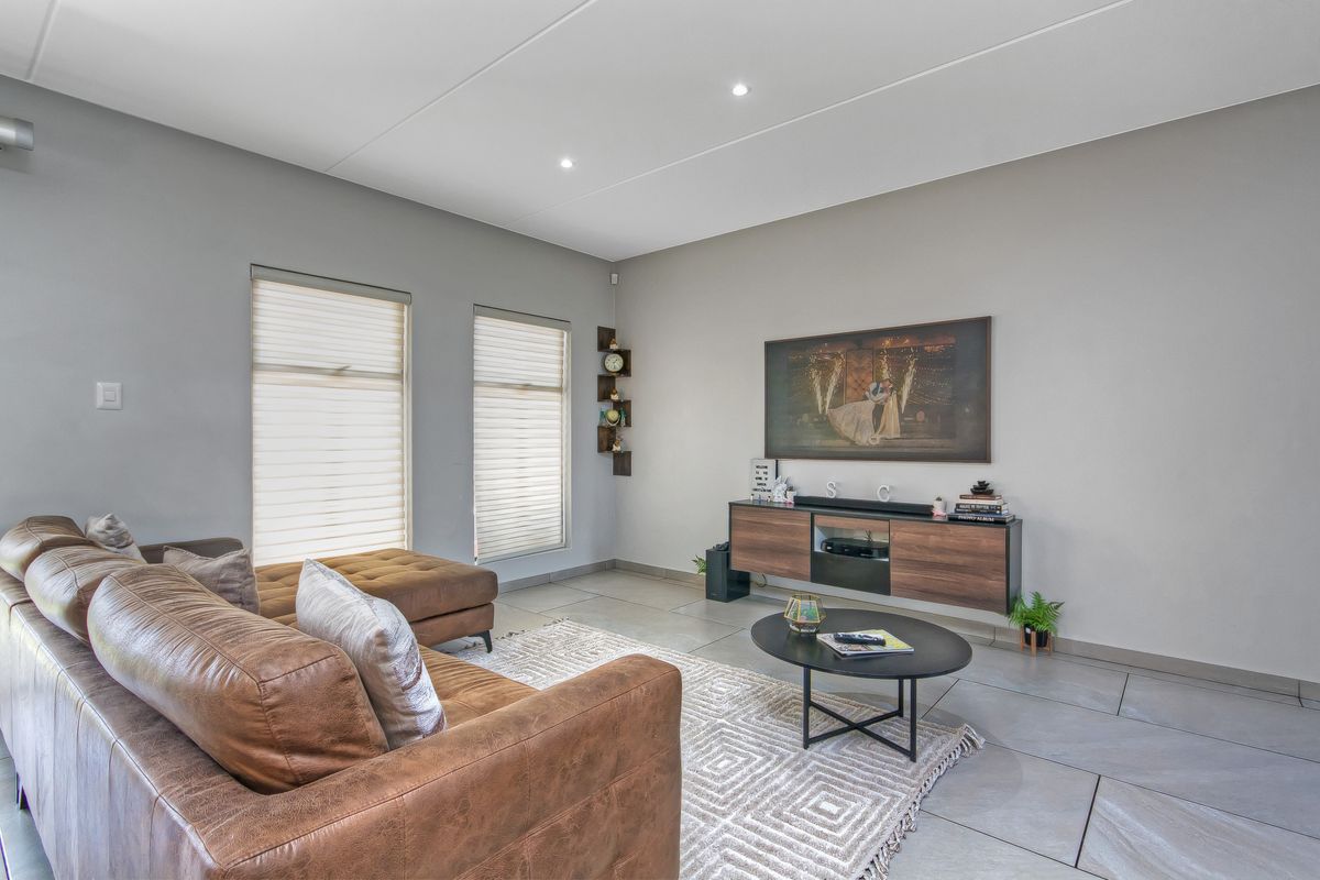 A modern, well-lit living room featuring large format floor tiles, recessed ceiling lighting, and dual windows with fitted roller blinds.