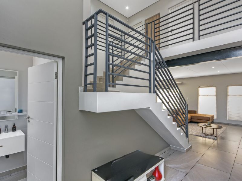 Modern entrance hallway featuring a sleek staircase with metal balustrades, tiled flooring, and access to a contemporary guest bathroom with a wall-mounted vanity.
