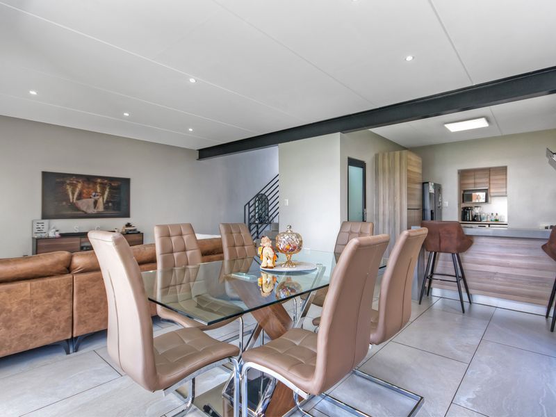Spacious open-plan living and dining area featuring modern tiled floors, an exposed steel beam, and a contemporary kitchen with a breakfast bar.