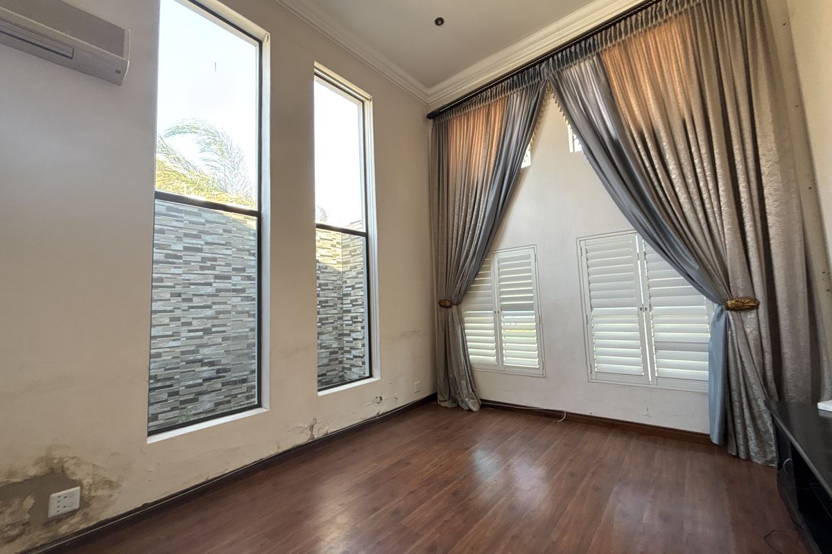 Spacious living area featuring high ceilings, tall windows, plantation shutters, and laminate flooring, currently showing signs of wall moisture damage requiring repair.
