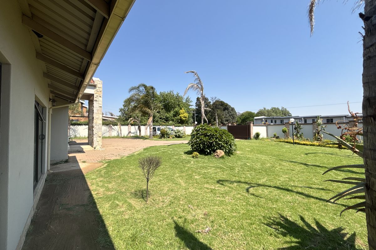Spacious rear garden featuring a well-maintained lawn, paved driveway area, and a covered patio accessible via sliding glass doors.