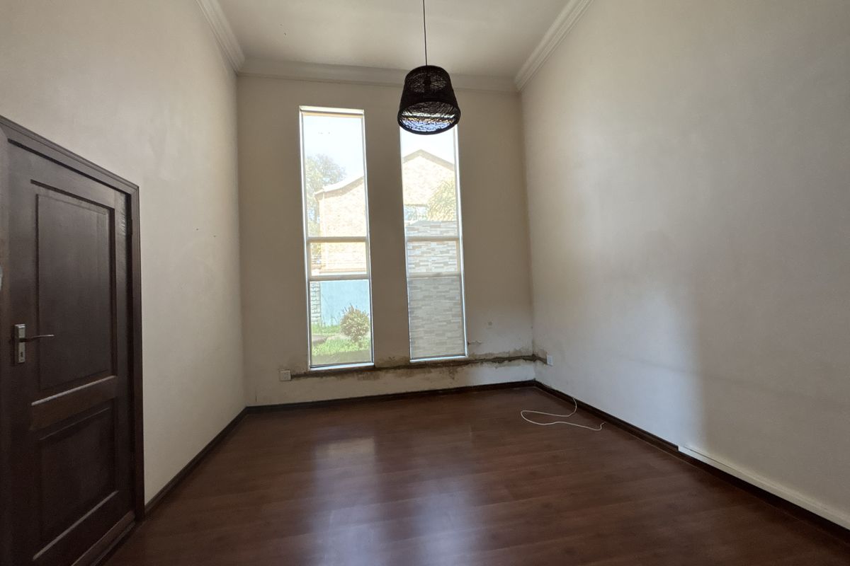 An empty bedroom featuring laminate flooring, tall windows, and coving, currently showing signs of wall plaster damage below the window frames.
