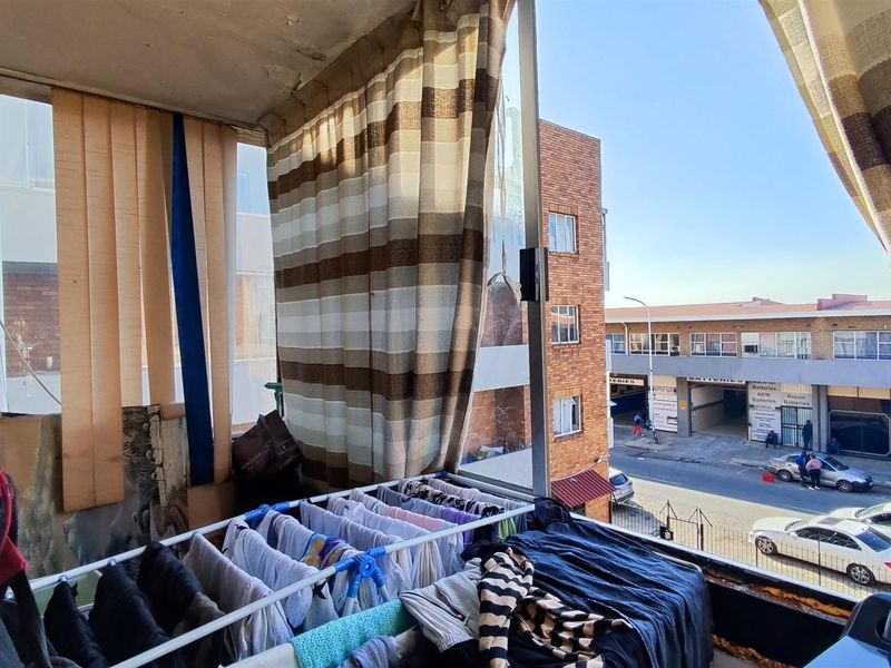 An enclosed balcony area featuring a street view, showing signs of wear on the ceiling and window frames.