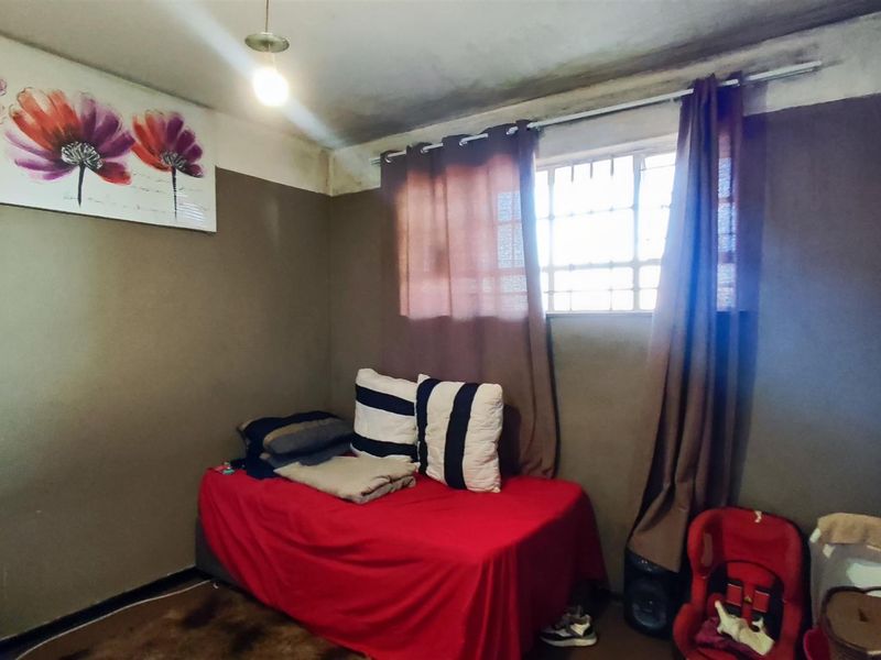 A bedroom featuring a window with security bars and a ceiling light fixture, currently showing signs of wear on the ceiling.