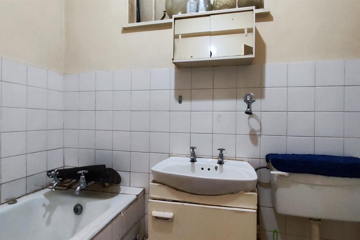 A dated bathroom featuring a bathtub, pedestal sink, and wall-mounted medicine cabinet, requiring significant modernization and repair of fixed finishes.