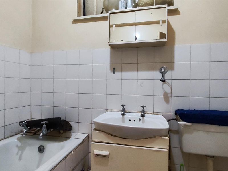 A dated bathroom featuring a bathtub, pedestal sink, and wall-mounted medicine cabinet, requiring significant modernization and repair of fixed finishes.