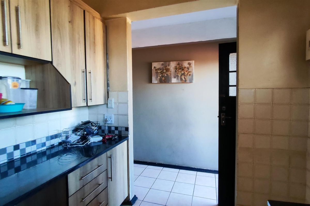 A functional kitchen featuring laminate cabinetry, granite countertops, and tiled backsplash, leading into an adjacent tiled hallway area.