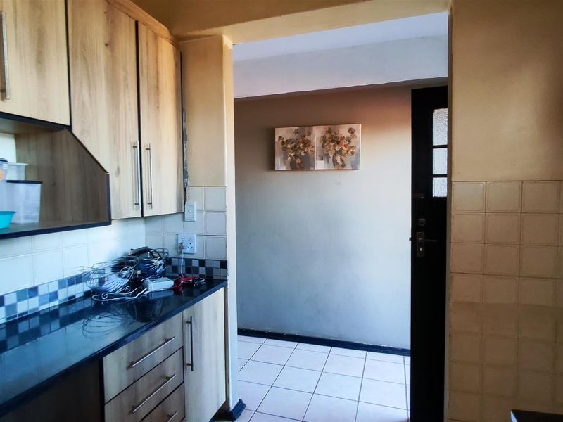 A functional kitchen featuring laminate cabinetry, granite countertops, and tiled backsplash, leading into an adjacent tiled hallway area.