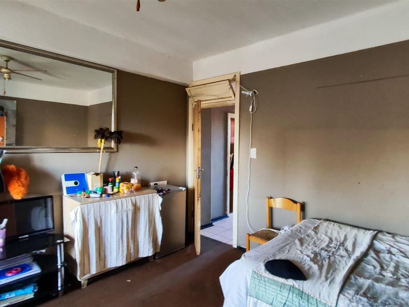A bedroom featuring a ceiling fan and wall-mounted mirror, requiring cosmetic updates to the wall finishes and flooring to improve its overall condition.