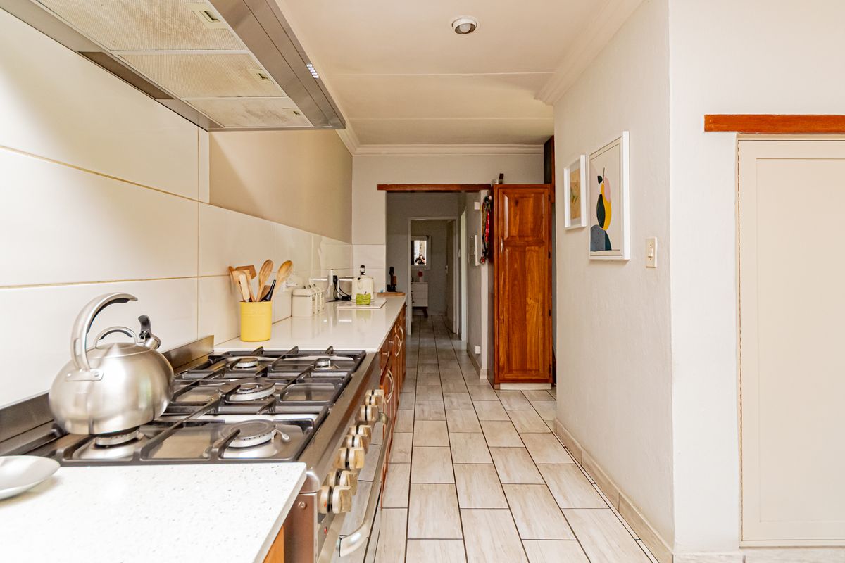 A functional kitchen featuring a gas stove, extractor fan, stone countertops, and tiled flooring, leading into a hallway with built-in storage.