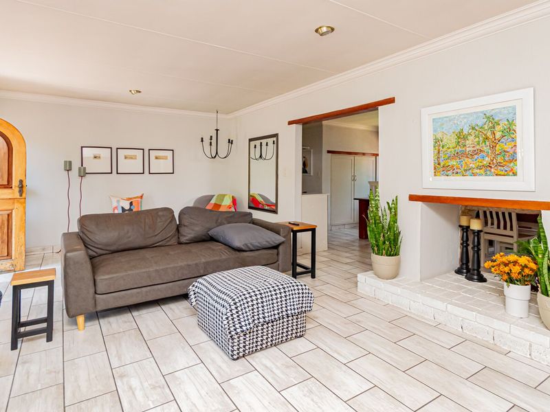A bright living room featuring a brick fireplace, tiled flooring, and a distinctive arched wooden entrance door, leading into an adjacent kitchen area.