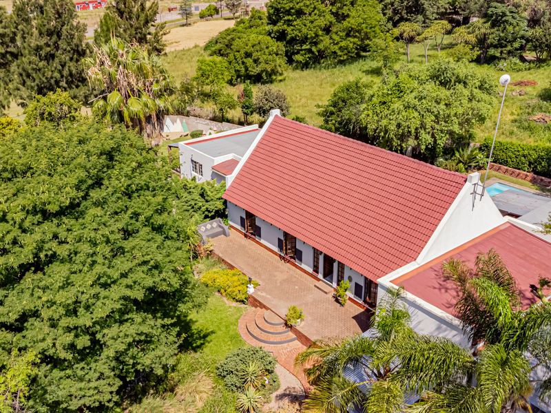 Aerial view of a small holding property featuring a main dwelling with a tiled roof, expansive brick patio, swimming pool, and established garden surroundings.